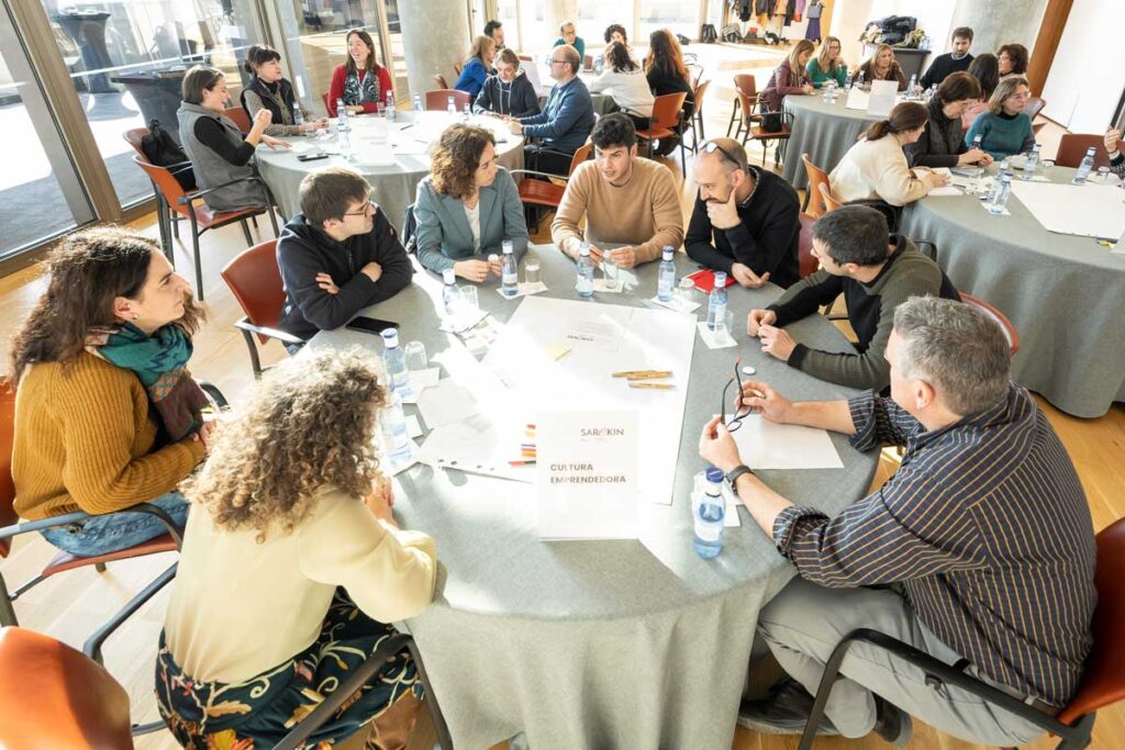 5 mesas de trabajo con varias personas departiendo en torno a ellas